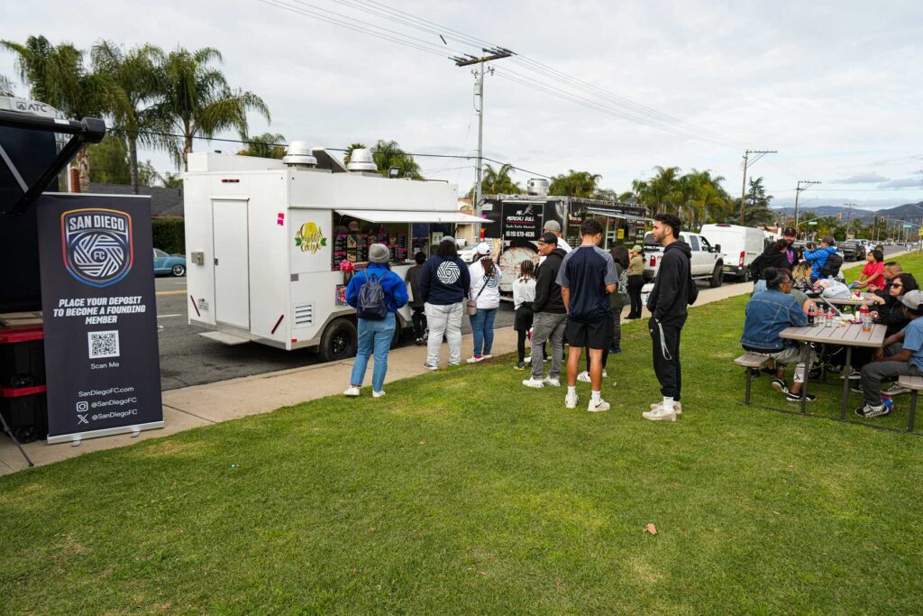 a group of people in line at a food truck outdoors 
